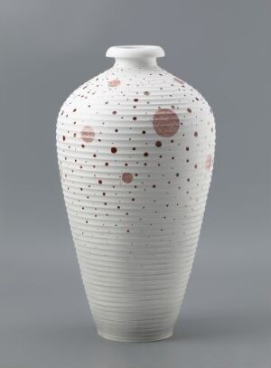  A tall white ceramic vase with horizontal ribbing and a sparse pattern of red dots, displayed against a neutral background.