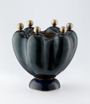  An ornate dark blue vessel with stylized petal-like indentations and golden finials on top, mounted on a slightly darker base, against a light background. Artist name and title are unknown.