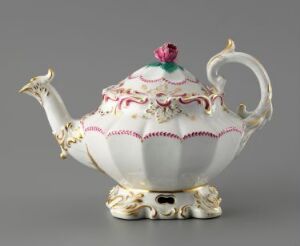  An ornate porcelain teapot with a creamy white base, delicate pink and gold designs, a stylized floral finial in deep pink and green on the lid, and intricate floral motifs in pink, green, and blue around its body, set against a neutral grey background.