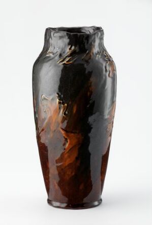  A tall, glossy vase with a blend of dark brown and amber colors, exhibiting a reflective and fluid-like quality on its surface. The artist's name and title are unknown.