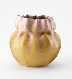  A small, mustard yellow ceramic vase with folded peach-toned edges dripping with rosy pink glaze on a white background.