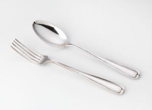  Two pieces of silver tableware, a spoon, and a fork, designed by Jacob Tostrup Prytz, are laid out on a light background. They showcase a simple, elegant design with polished surfaces, displaying a high-quality silver finish.