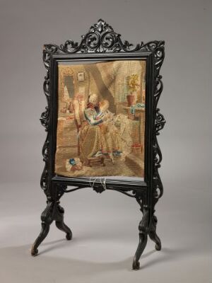  An intricately carved, dark-colored picture frame on a decorative easel displays a painting of figures in historical attire, embodying a baroque or rococo style.