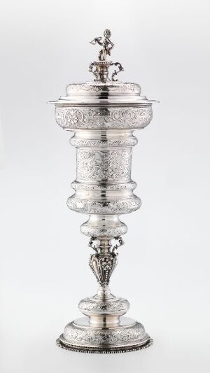  A tall, ornately crafted silver trophy named "Pokal" by artist Johannes Johansen d.e. Reimers, featuring a wide decorative base, an embellished stem, a fluted body with intricate design work, and a domed lid topped with a decorative finial, all rendered in polished silver.