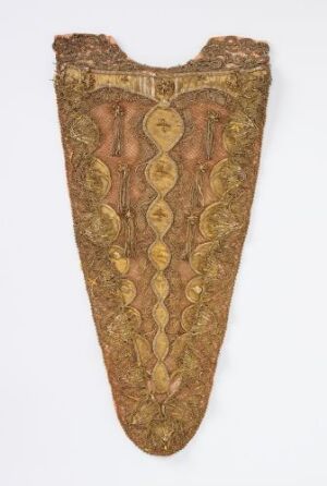  An image of an ornate, aged golden-brown fabric piece with a design featuring a central axis of interlocking loops flanked by symmetrical leaf-like motifs within a decorative border, giving a sense of antique craftsmanship. The top edge is square with a slight inward curve, and the bottom comes to a pointed tip, resembling a slender, inverted cone or shield.