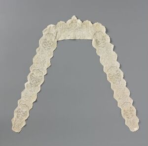  An off-white, intricately designed floral lace collar laid out in a V-shape against a light grey background.