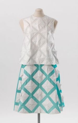  Sleeveless top and skirt costume displayed on a mannequin, designed by Carlos Zachrison. The white top features a quilted texture, while the knee-length skirt showcases a turquoise and white geometric diamond pattern with turquoise ribbon accents.