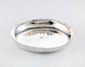  A polished silver piece titled "Underfat" by Jacob Nilsen, reflecting light on its smooth, curved surface, showcasing the craftsmanship of embossed silver used in serving and consuming food.