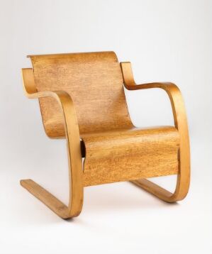 
 An elegantly designed Alvar Aalto rocking chair crafted from form-bent laminated birch veneer, showing warm honey colors with visible wood grains and smooth, flowing lines indicative of Scandinavian design.