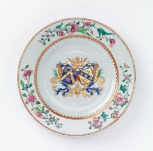  An ornate porcelain plate with a white background featuring a central coat of arms with a blue and gold cross design, surrounded by golden detailing and a border of small red and pink flowers with green leaves on the rim.