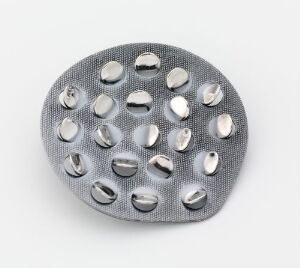  Oxidized sterling silver brooch by J. Tostrup with a pebble-like, oval shape showcasing a grid of polished convex domes on a textured, darker silver background, creating a play of light and contrast.