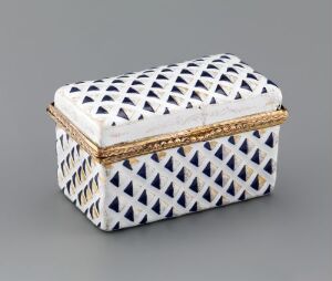  A rectangular, ceramic or enameled trinket box with a blue and white harlequin pattern and a gold or brass metal rim on the lid.