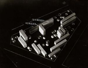  Monochromatic photo with architectural composition of various geometric shapes, including central rectangular blocks and scattered spheres, all in different shades of gray, evoking a sense of an abstract miniature cityscape.