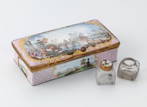  A small, decorative rectangular box painted in pastels with an 18th-century garden scene on the lid, accompanied by a miniature glass jar with a label and metal cap, and another lone metal cap, all displayed against a light grey background. Artistname and title unknown.