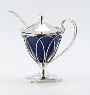  An elegant small silver mustard pot with a cobalt blue glass or ceramic body, featuring a silver frame with a curved handle and a reflective surface, accompanied by a silver spoon partially inserted into the pot, set against a plain white background.