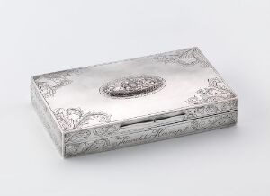  An antique silver rectangular box with intricate floral engravings on its surface, featuring a central polished oval medallion on the lid, set against a soft light gray-white background.