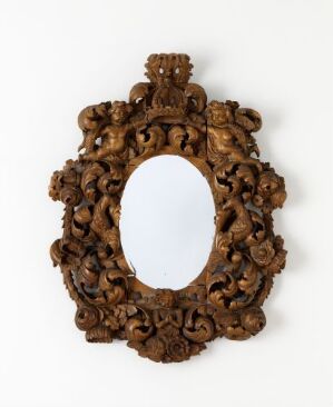  An antique carved wooden frame with a central oval aperture, surrounded by detailed scrollwork and decorative motifs, including a figure that resembles a cherub at the top. The frame is against a plain, light background. Artist and title are unknown.