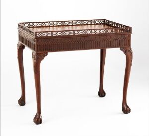  Antique mahogany table designed by Thomas Chippendale, featuring delicate carvings, lattice edge detailing, and shapely legs ending in ball-and-claw feet, displayed against a light background.