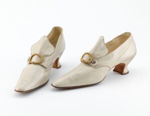  A pair of vintage cream-colored women's shoes with golden buckles and modest brown heels on a white background.