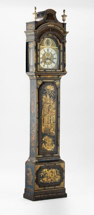  An antique grandfather clock with dark wood and gold inlay detailing, standing against a white background. The clock features an arched face, an intricate pediment at the top, and decorative gold panels on the body and base.