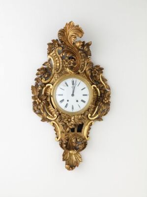  An intricately carved and gilded Rococo-style wall clock titled "Veggur" by an unidentified artist, featuring a white clock face with black Roman numerals and hands set within an ornate, golden framework with openwork details.