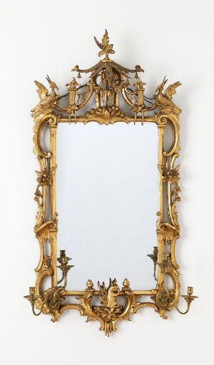  An elaborate baroque-style gilt mirror frame without the mirror, featuring intricate scrollwork, acanthus leaves, floral designs, and symmetrical crests, displayed against a neutral wall. Artistname and title are unknown.