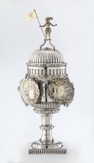  An ornate silver drinking vessel by artist Jacob Steen, featuring a reflective surface with engraved and chased decorations, embossed medallions on the body, vertical ribs on a dome-shaped lid, and a small figurative sculpture on top, all suggesting antique luxury design.