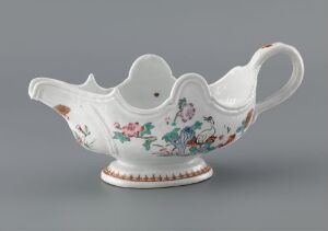  A traditional porcelain gravy boat with a white base adorned with delicate floral patterns in soft pastels, featuring a round base and a bird-like shape, on a neutral gray background.