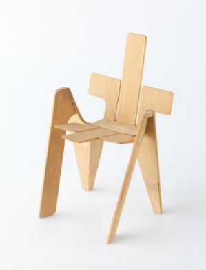  A minimalist wooden chair with an unconventional design featuring a tall, flat backrest and geometric shapes, set against a white background.