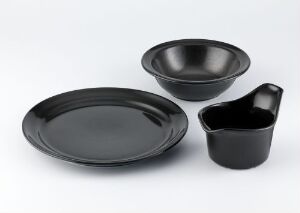  A set of sleek, matte black porcelain tableware titled "Glohane" by Porsgrunds Porselænsfabrik AS, including a flat round plate, a deep round bowl, and a handled pouring jug, displayed on a neutral background.