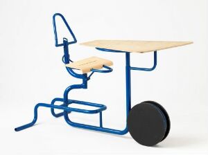  "Ekstrem-elevpult og stol," a modern student desk and chair design by Terje Ekstrøm featuring a light wood laminated seat and desk surface, with a bold blue lacquered steel frame, and a large black wheel attached to the front of the desk for mobility.