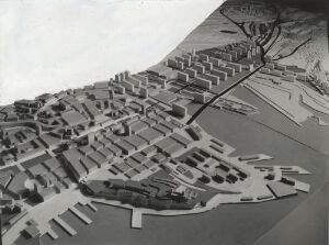  A black and white photograph of an architectural model depicting an organized city layout with various building shapes, a tree, and a backdrop of a hillside, signifying the contrast between man-made constructions and natural landscapes.