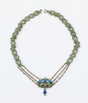  An elegant two-tiered necklace featuring an upper string of vibrant green leaves and lower strands of fine silver chains. The centerpiece is a circular, colorful design with blue, green, and hints of red and yellow, from which hangs a blue tassel.