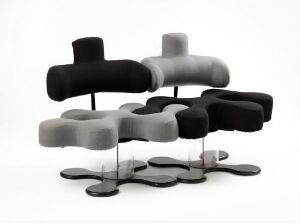 
 "Ekstrem Puzzle," a furniture piece designed by Terje Ekstrøm, featuring abstract black and grey cushioned elements with an organic shape, supported by bent metal legs above a flowing base, exemplifying modern design.