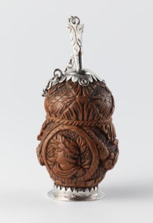  An ornate carved bottle with a warm brown body showcasing intricate floral-like motifs, topped with a hinged silver metallic cap with a loop, set against a plain background. Artistname and title are unknown.