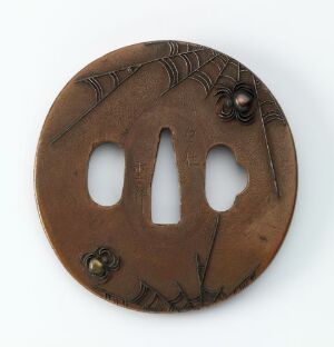  A circular brown object with three large oval holes in the center and artistic carvings on the surface, including two small raised, darker features, set against a neutral background.