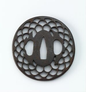  A round, dark-colored metal tsuba (Japanese sword hand guard) with an intricate, openwork petal pattern and a central three-leafed symbol, against a light background.