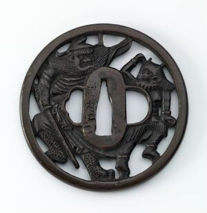  A circular, dark metallic ornament with intricate carvings featuring a central kanji character and surrounding mythological creatures. The object is possibly a Japanese tsuba, with a detailed openwork design set against a neutral background.