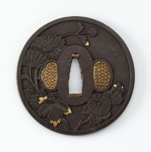  A round, dark brown tsuba (Japanese sword guard) with a central oval cut-out and decorative relief of floral patterns highlighted in gold against a dark background.