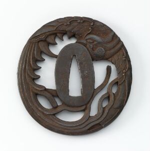  A circular dark brown wooden carving with an oval center cut-out and symmetrical, leaf-like designs, set against a neutral grey background.