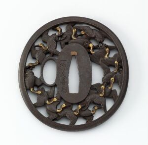  An ornate, circular, possibly Japanese, iron tsuba with gold accents and an intricate openwork design featuring clover-like motifs and a central elliptical hole, set against a plain light grey background.