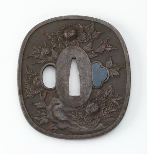  An antique Japanese tsuba with dark patinated metal, intricate foliage engravings, and a central elliptical blade opening with a heart-shaped silver inlay on one side against a white background.