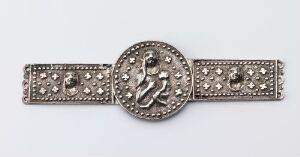  A decorative metal belt with a central circular medallion featuring an embossed figure in profile, flanked by symmetrical straps with embossed stars and geometric shapes on a light grey background.