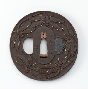  An intricately designed Japanese tsuba (sword handguard) with golden highlights on a dark brown, possibly iron, background. The tsuba displays a chrysanthemum flower pattern and has a central opening for the sword blade and a smaller side notch for accessories.