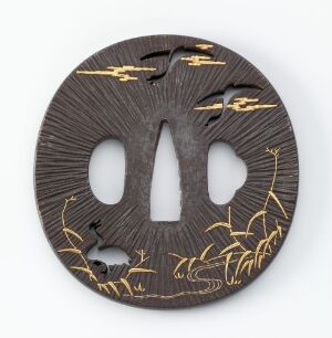  A round, slate gray object with radial lines and golden illustrations of herons and reeds, featuring two symmetrical keyhole-shaped cutouts in the center.