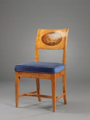  A wooden chair with light golden-brown frame and royal blue upholstered seat with tufted detailing. The chair features an oval-shaped inset in the backrest showcasing a variegated brown wood pattern, presented against a neutral grey background. Artistname and title are unknown.