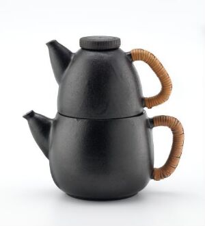  A matte black, high-fired ceramic teapot designed by Eva Børresen with a sleek modern shape and a handle and lid knob wrapped in light brown, fletted peddig material, highlighting a contrast of color and texture against the dark body of the teapot.