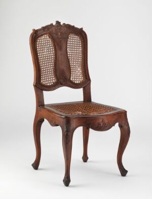  "Stol," a chair made from stained and varnished walnut wood with carved decorative elements and cane webbing back and seat, featuring curved legs and a loose plush cushion by an unidentified artist.