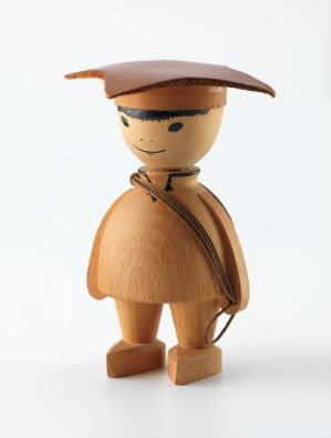  A wooden figurine titled "Gutt i samisk drakt" by Hans Brattrud, showcasing a boy in traditional Sami dress, featuring a four-pointed hat, warm honey-toned beechwood body with simple facial features, a dark brown neck cord, and painted cultural details on a plain white background.