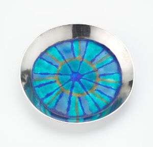 
Alt-Text: A round, decorative dish with a metallic silver rim and a stained-glass pattern featuring a radiant starburst design with vibrant shades of blue and turquoise.